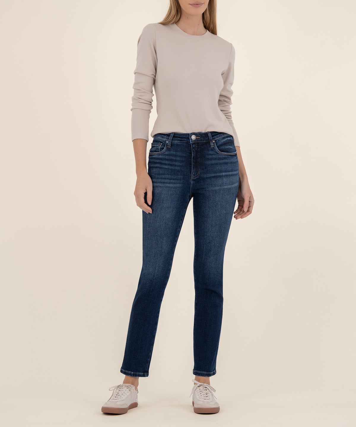 Woman wearing dark blue straight-leg ankle jeans with a high rise and rolled hem, paired with a beige long-sleeve top.