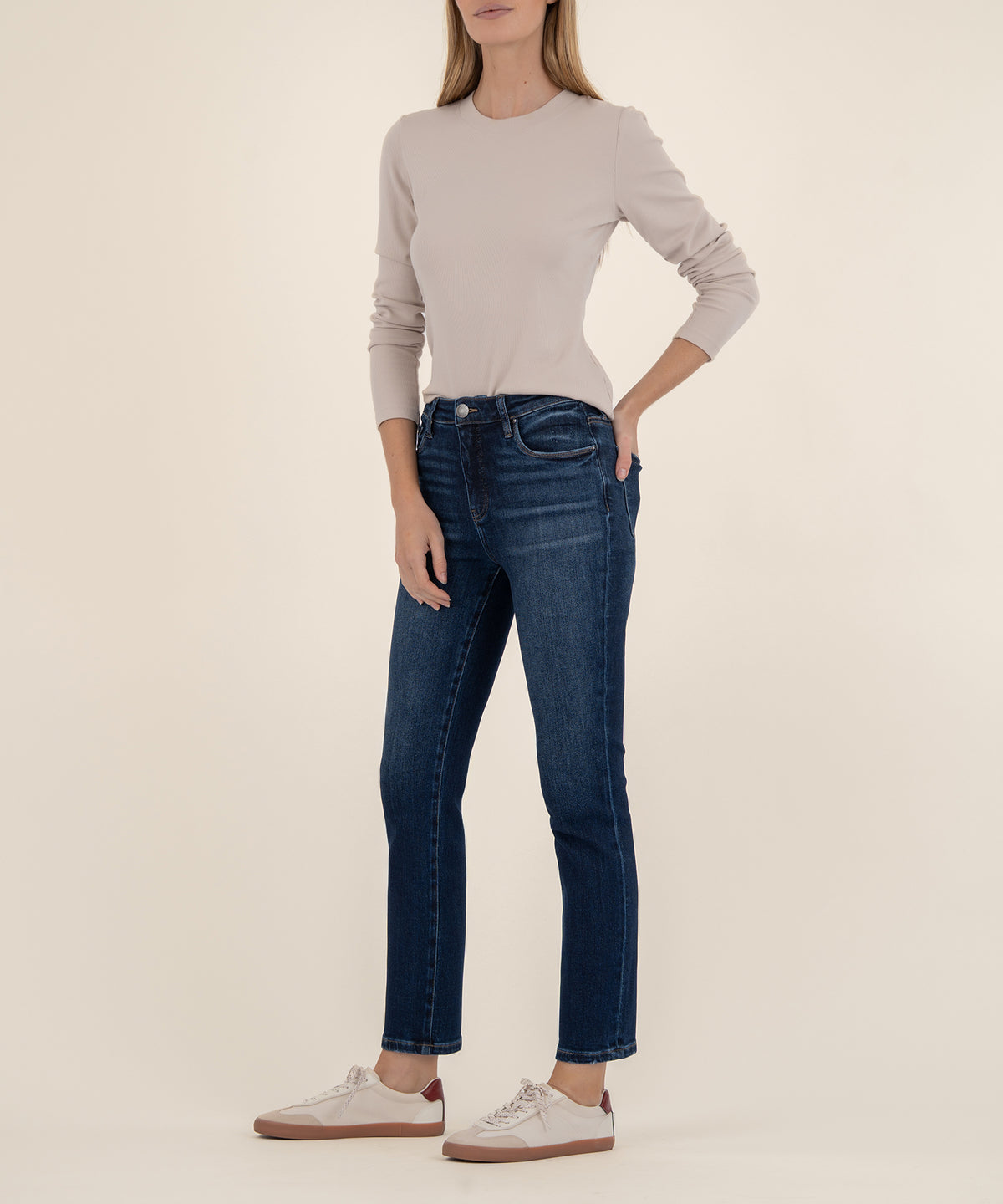 Woman wearing dark blue ankle straight leg jeans with cream long-sleeve top and white sneakers.