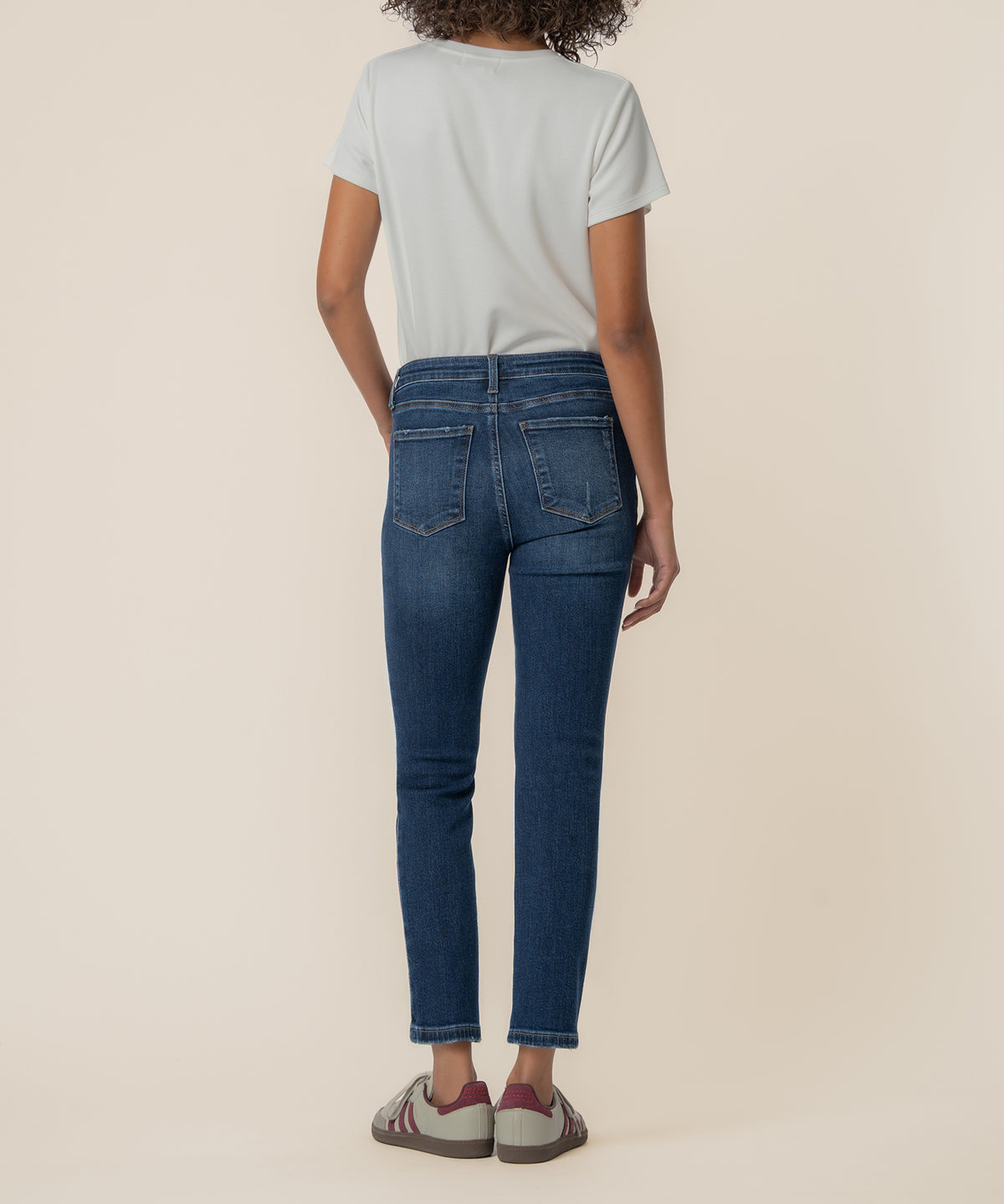 Woman wearing white t-shirt and dark blue high-rise straight ankle jeans with cropped hem, back view.