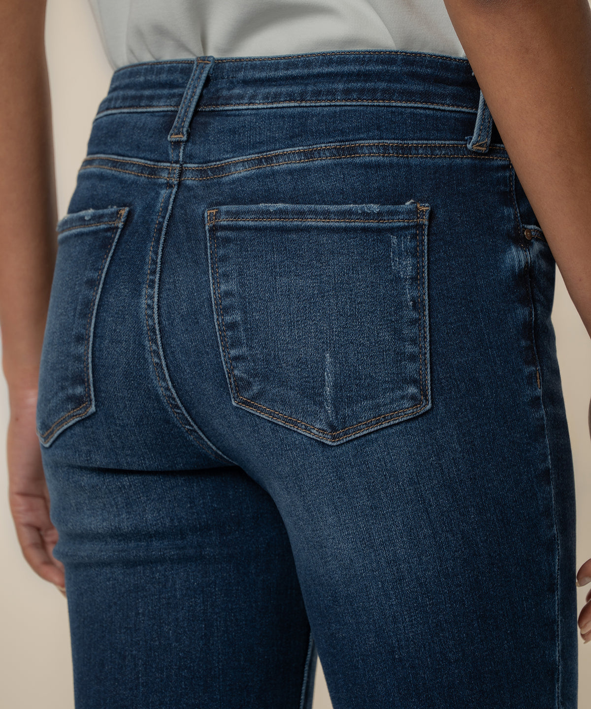 Rear view of dark blue denim jeans with high waist, straight leg, and back pocket detail on model wearing white tank top.