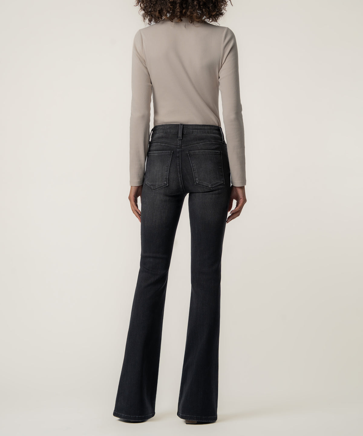 Rear view of a person wearing faded black high-rise flare jeans with back pockets and a fitted beige long-sleeve top.