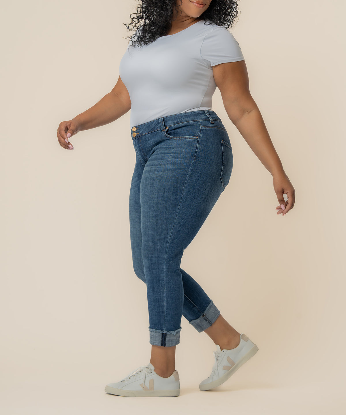 Woman wearing light blue t-shirt and cropped blue jeans with rolled cuffs and gold button details.