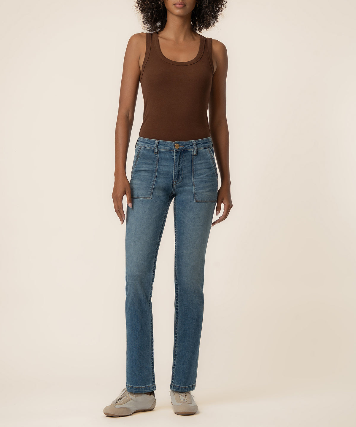 Medium wash high-rise straight leg jeans with patch pockets, worn with a brown tank top and beige sneakers.