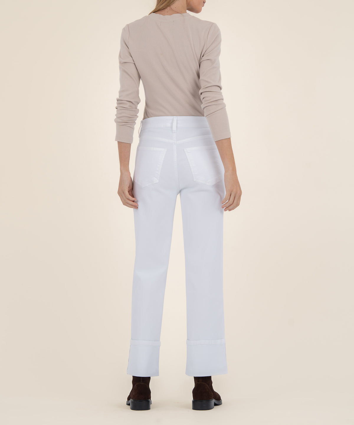 Rear view of a person wearing high-rise white wide-leg jeans with cuffed hems, a beige long-sleeve top, and dark brown boots.