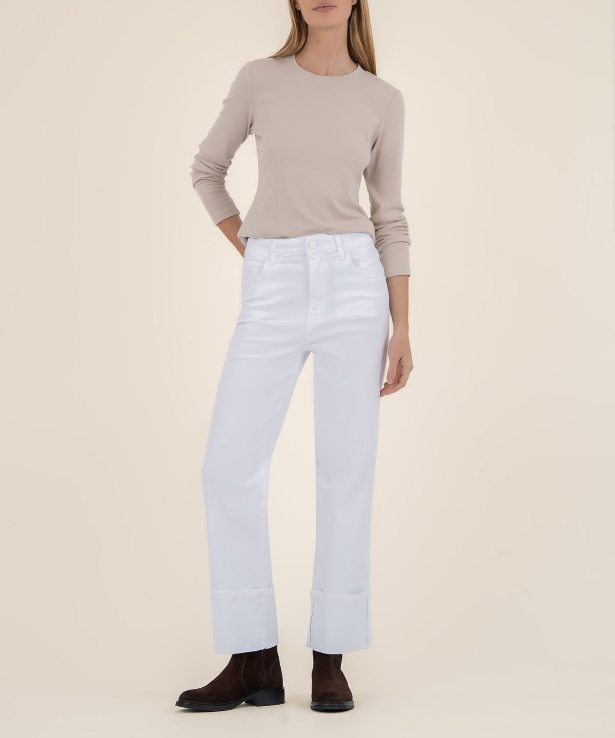 A woman wears high-rise white wide-leg jeans with wide cuffed hems, a beige long-sleeve top, and dark brown suede ankle boots.