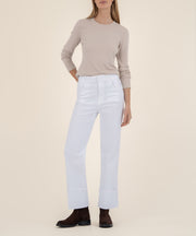 A woman wears high-rise white wide-leg jeans with wide cuffed hems, a beige long-sleeve top, and dark brown suede ankle boots.