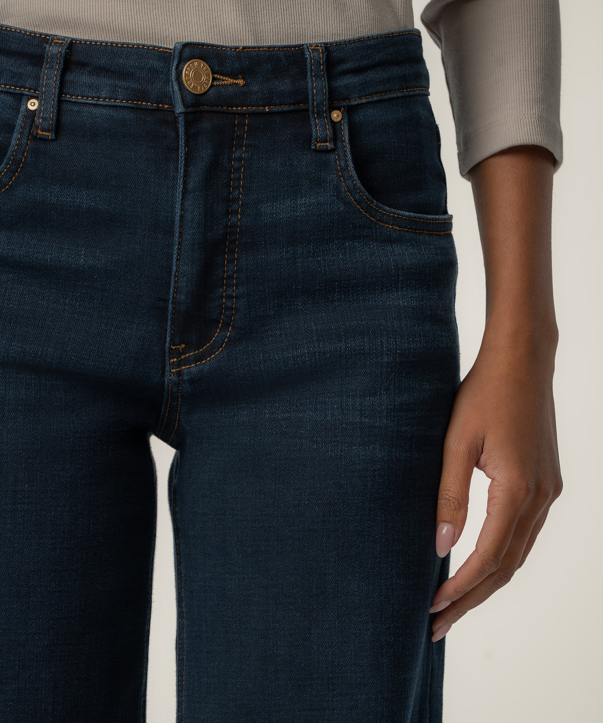Close-up of dark indigo high-rise wide-leg jeans with a gold button and copper stitching, worn with a gray ribbed top.