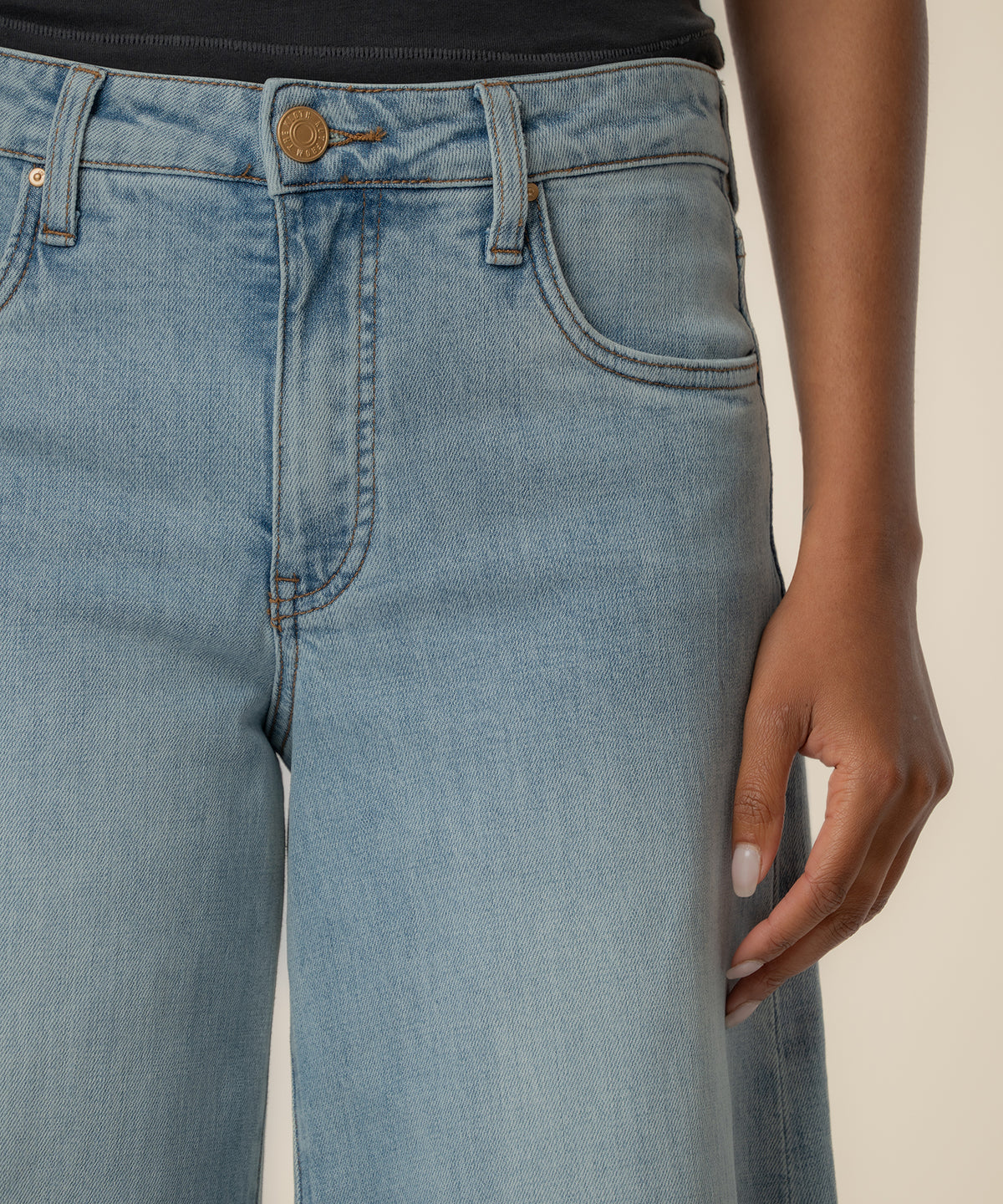High-rise light blue jeans with wide legs, brass button, and contrast stitching detail at the waistband.
