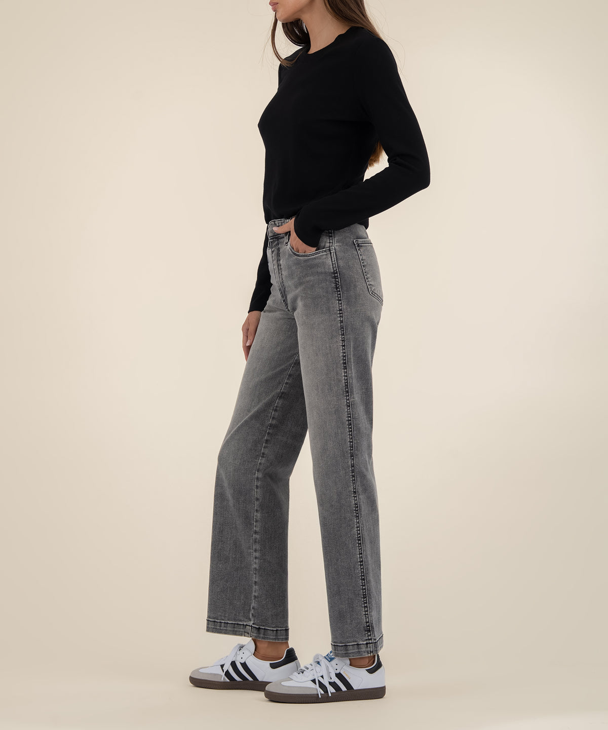 Woman wearing high-rise gray straight-leg jeans with black long-sleeve top and white sneakers with black stripes.