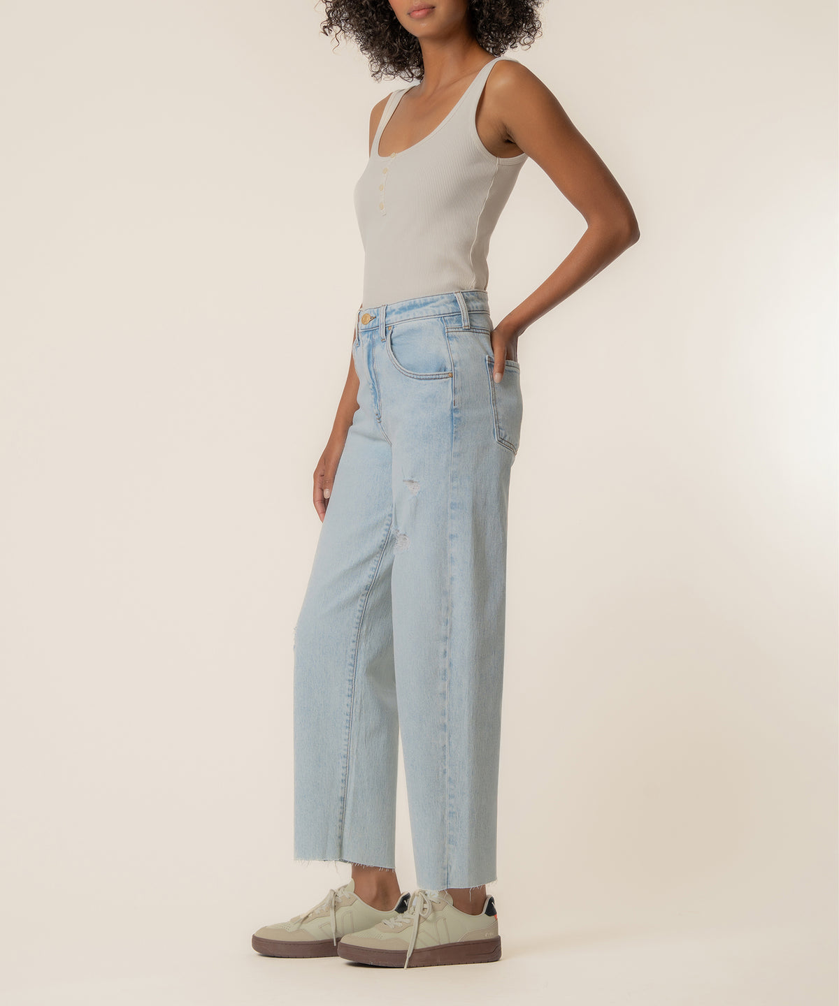 Woman wearing light blue high-rise wide-leg jeans with a white tank top and cream sneakers.