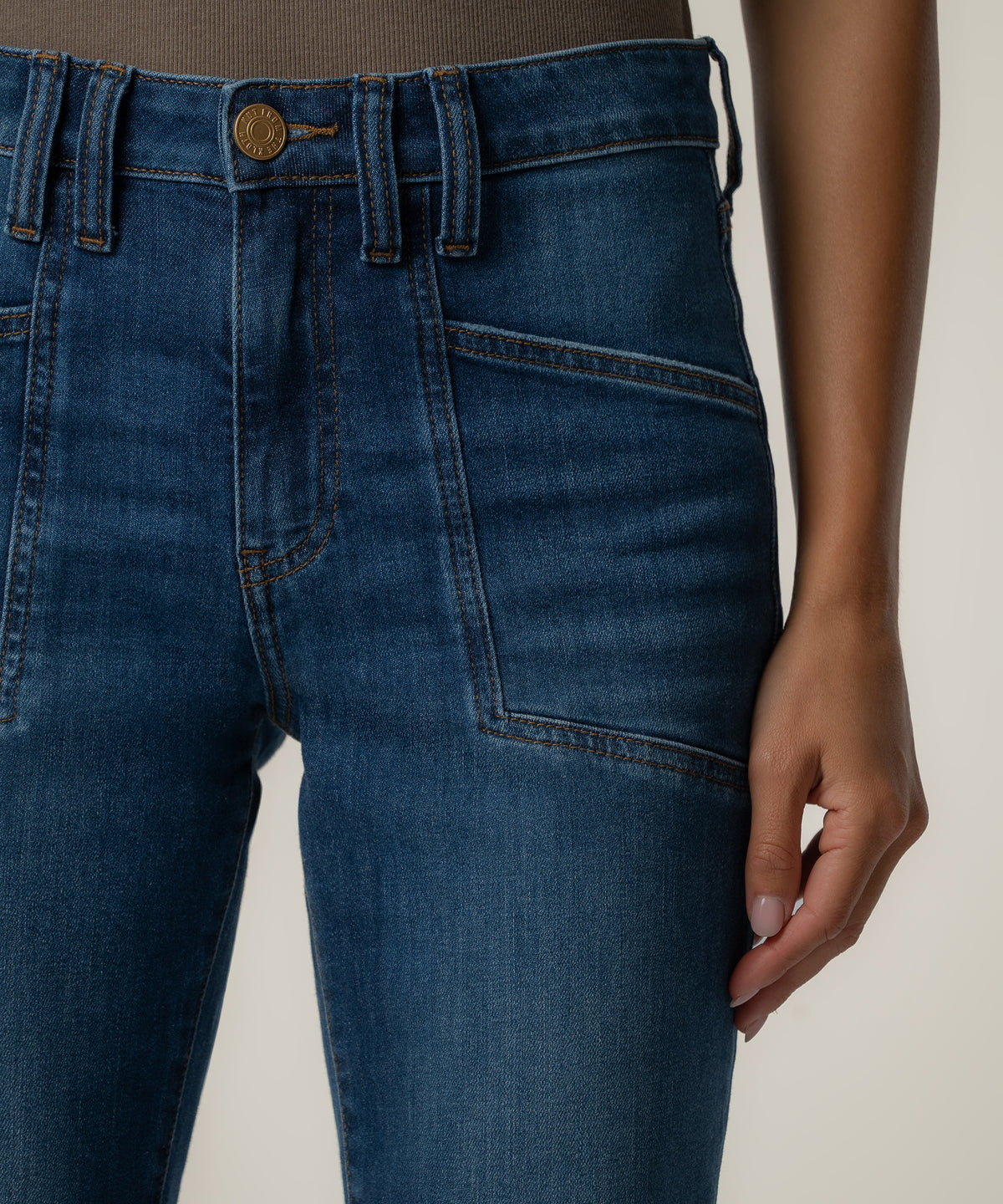 Close-up of a person wearing medium-blue high-rise jeans with a brass button, belt loops, and angled front patch pockets.