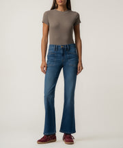 A woman wears medium-blue high-rise flared ankle jeans with large front patch pockets, a taupe fitted tee, and burgundy sneakers.