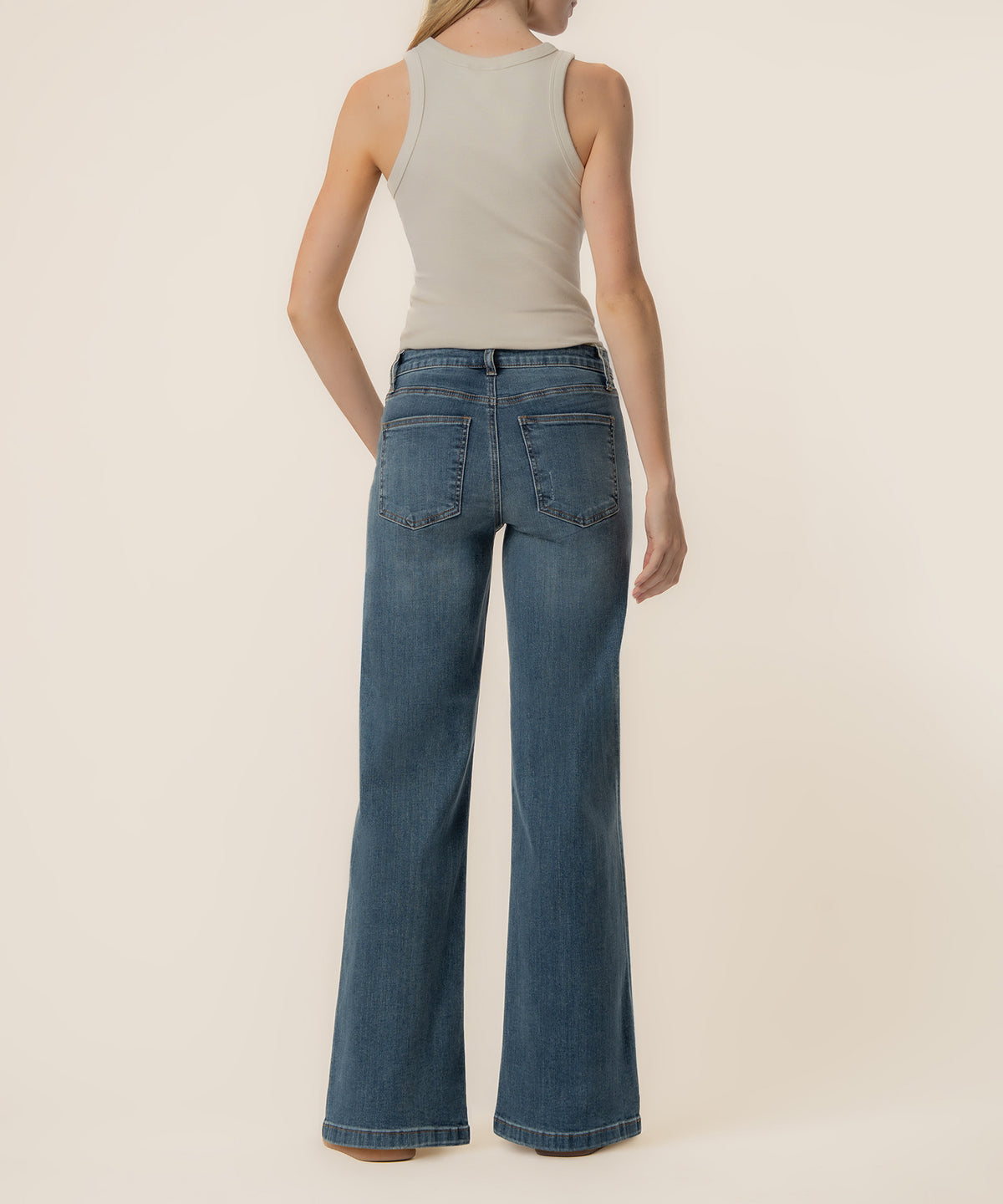 Woman wearing high-rise wide-leg jeans in medium blue wash with a cream sleeveless tank top.