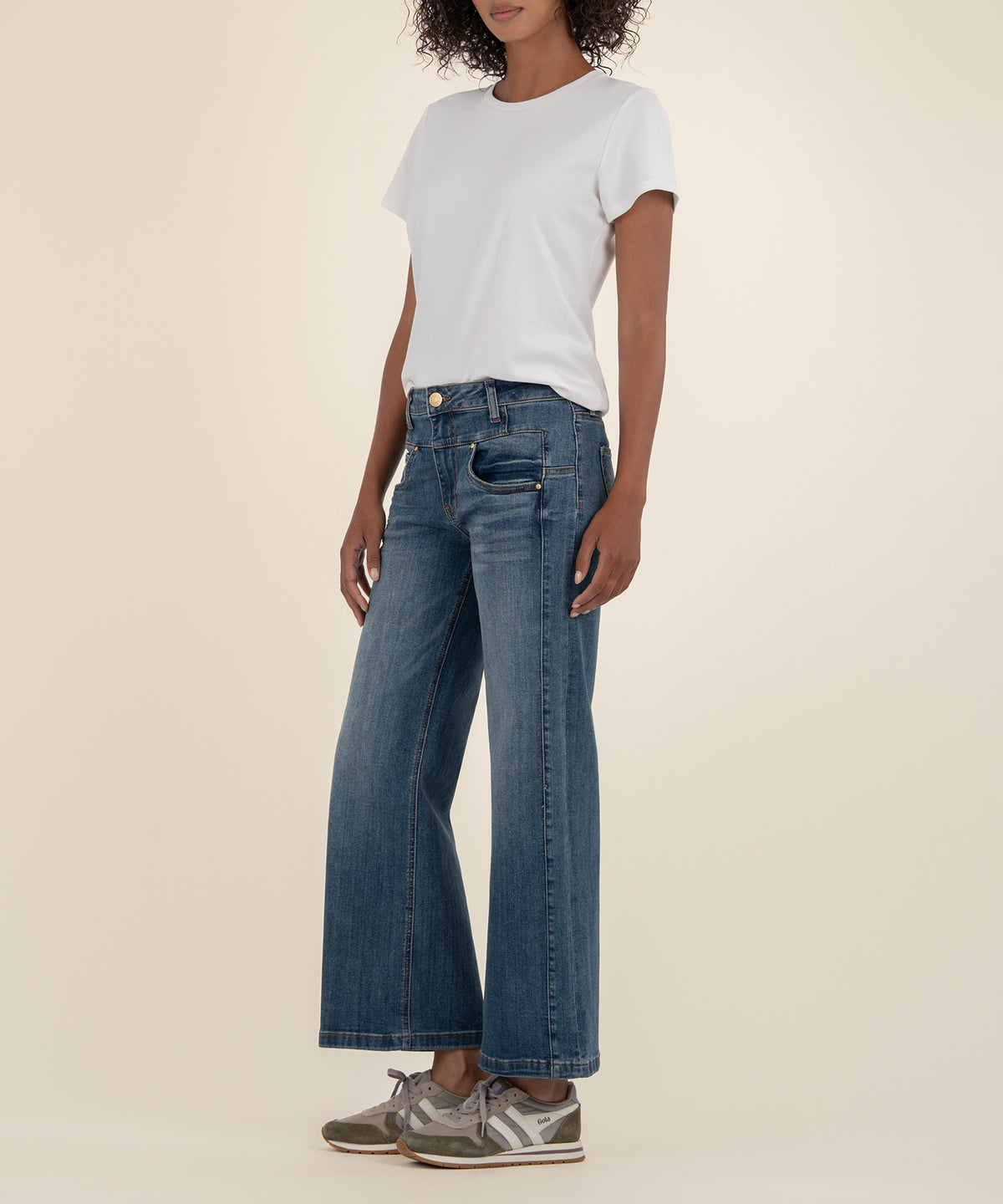 Woman wearing white t-shirt and blue high-rise wide-leg jeans with gold button detail.