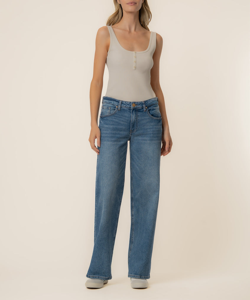 Woman wearing light beige tank top and medium-wash blue straight-leg baggy jeans with low rise.