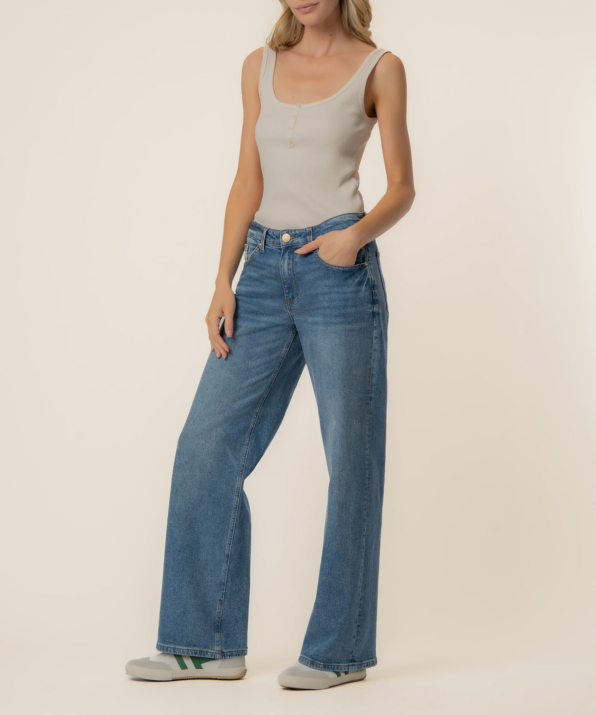 Woman wearing beige sleeveless tank top and blue baggy straight-leg jeans with low rise waistband.