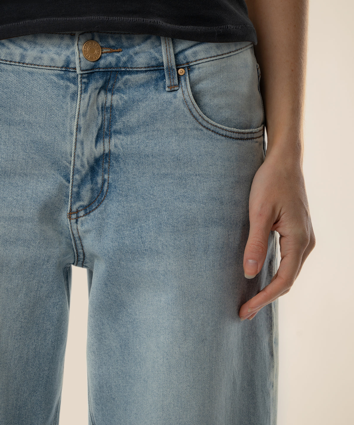 Light-wash baggy straight-leg jeans with power wash distressing and gold button detail on model.
