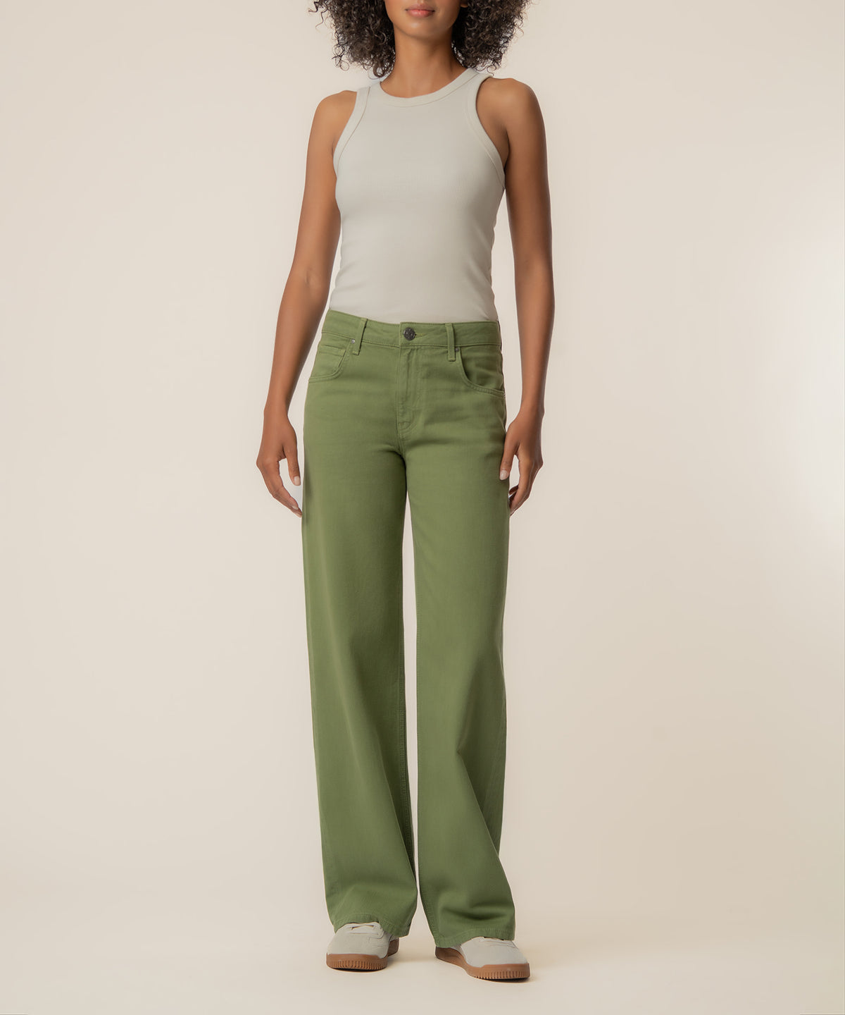 Woman wearing cream sleeveless tank top and sage green low-rise straight-leg jeans with white platform sneakers.
