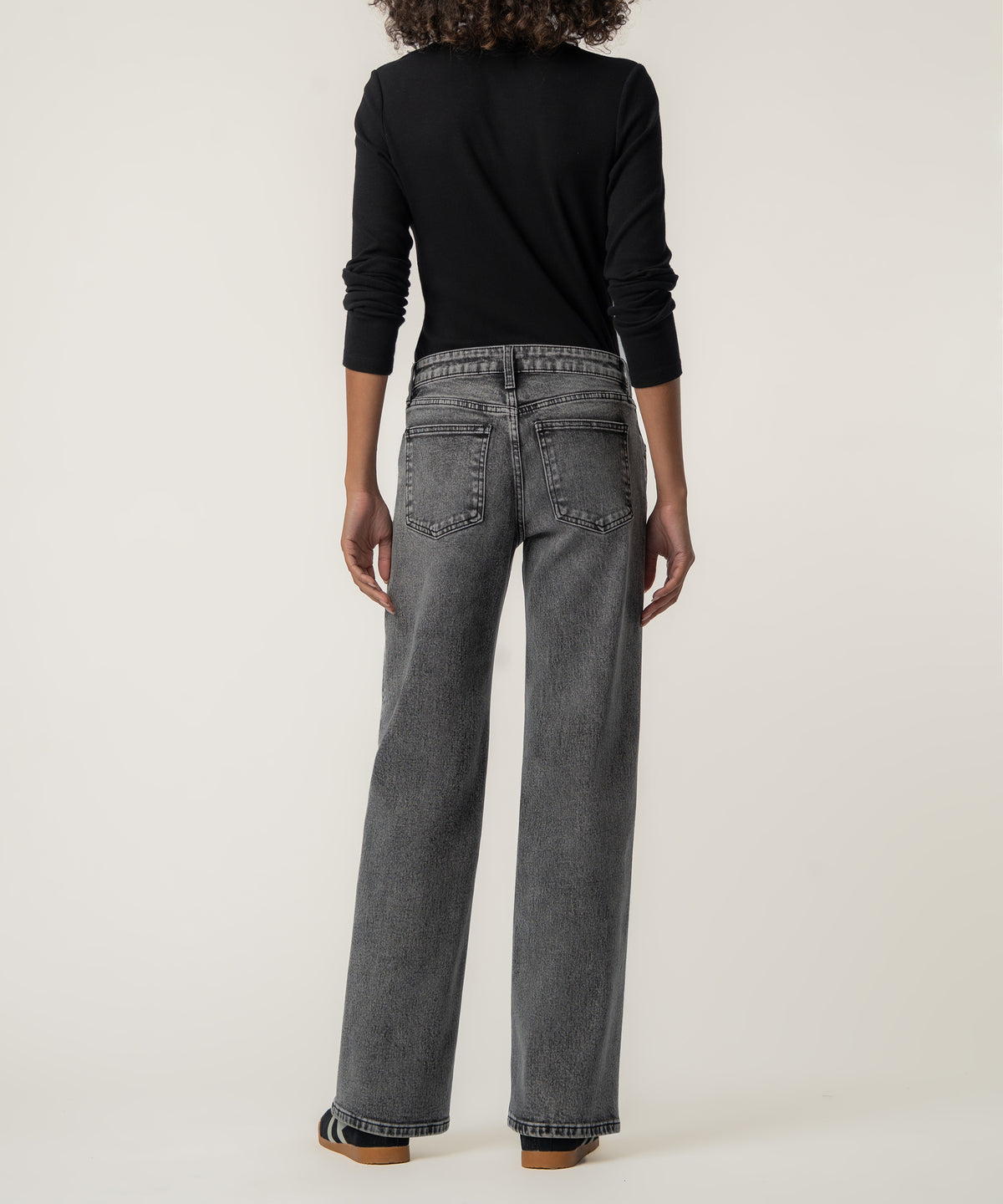 A person seen from behind wears faded gray straight-leg jeans with a black long-sleeve top and dark sneakers.