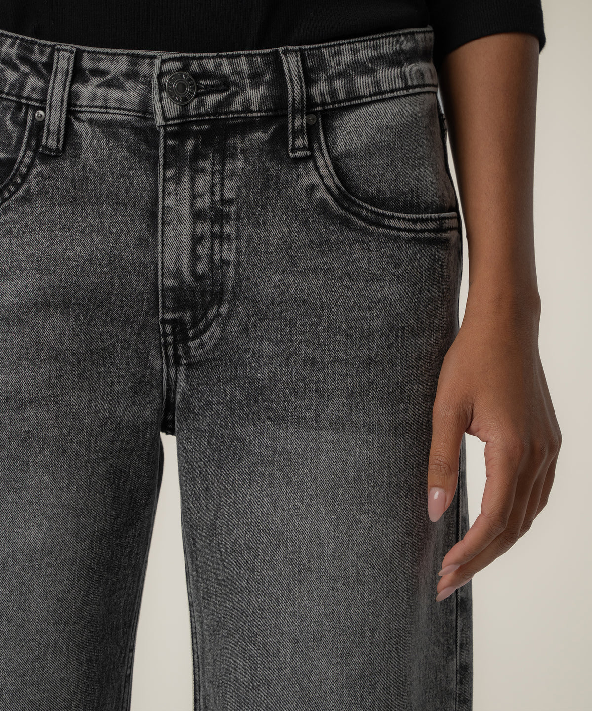 Close-up of a person wearing faded black low-rise straight-leg jeans with a button closure, belt loops, and a black top.