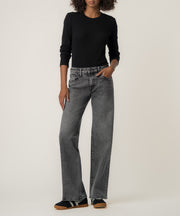 A woman stands against a neutral backdrop wearing faded gray straight-leg jeans, a black long-sleeve top, and dark sneakers with gum soles.