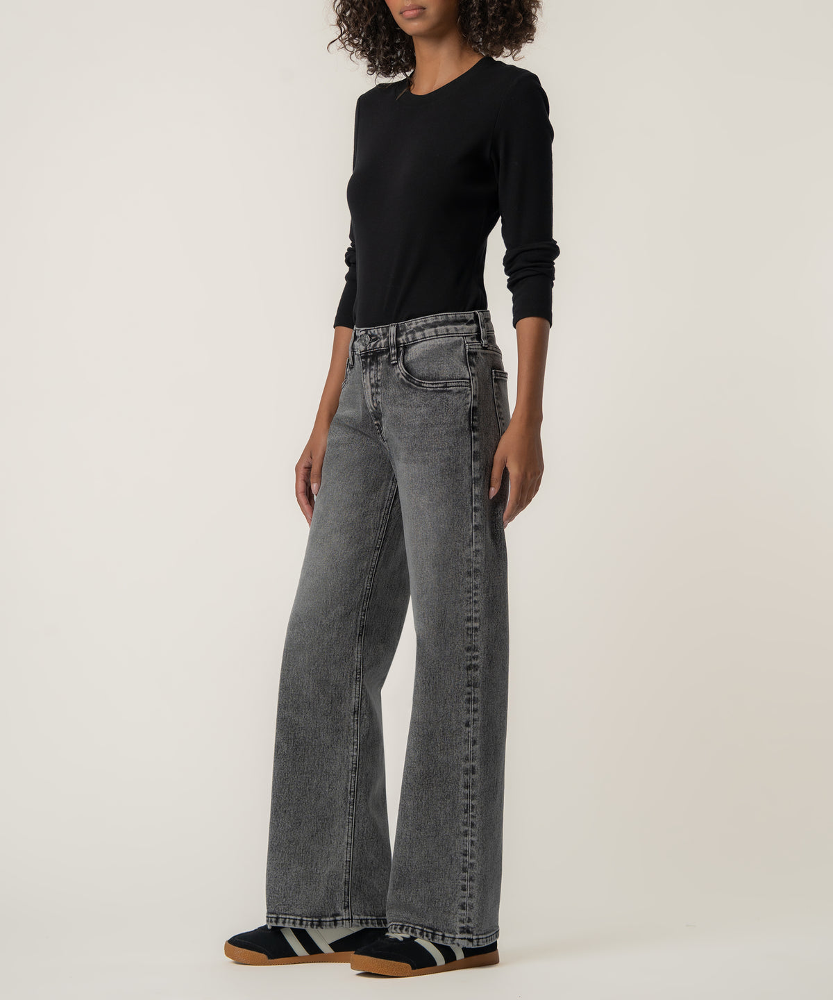A woman wearing faded gray wide-leg low-rise jeans with a black long-sleeve top and black sneakers with tan soles.
