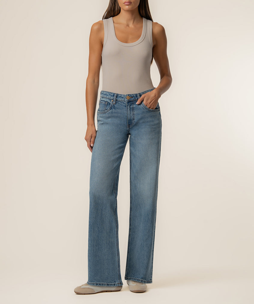 Woman wearing light gray sleeveless tank top and light blue wash baggy straight leg jeans with low rise.