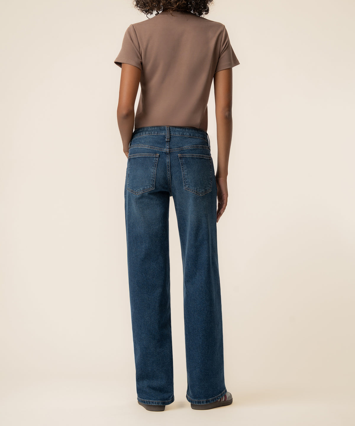 Blue denim baggy straight leg jeans with low rise waistband, shown from back view on model wearing brown t-shirt.