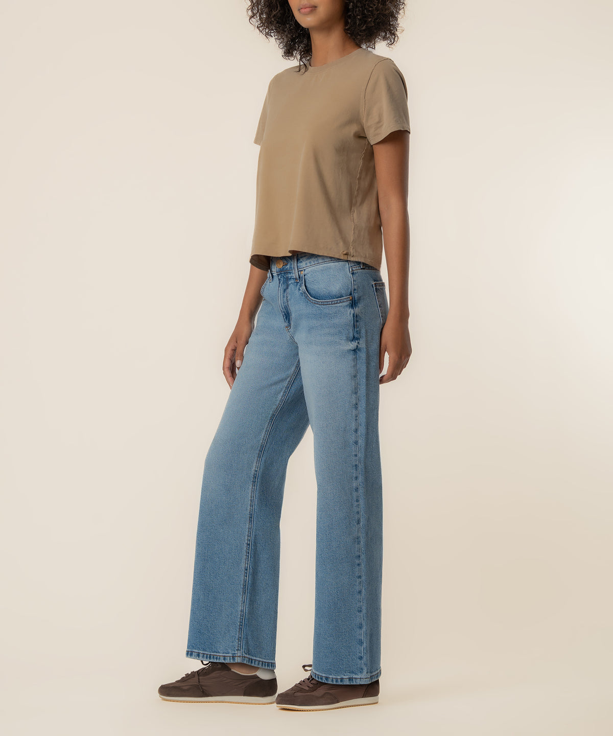 Woman wearing light blue baggy straight-leg jeans with low rise and a tan t-shirt.