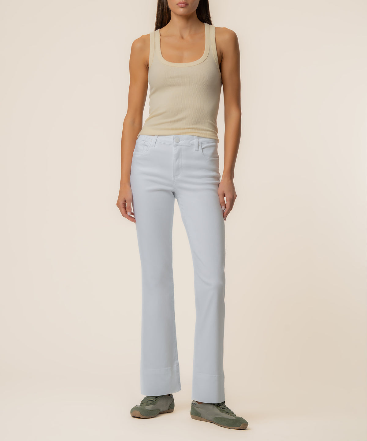 Woman wearing optic white mid-rise flare jeans with long inseam paired with a cream tank top.