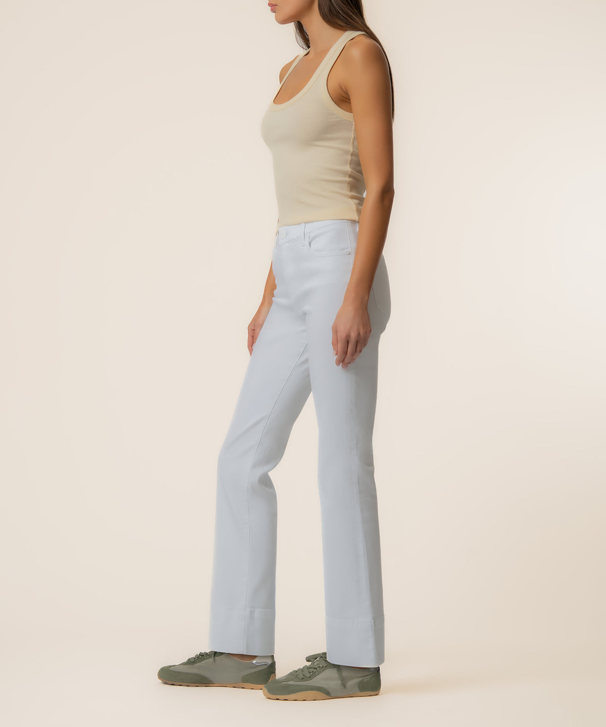 Woman wearing white ribbed tank top and light blue flare jeans with long inseam, side view.