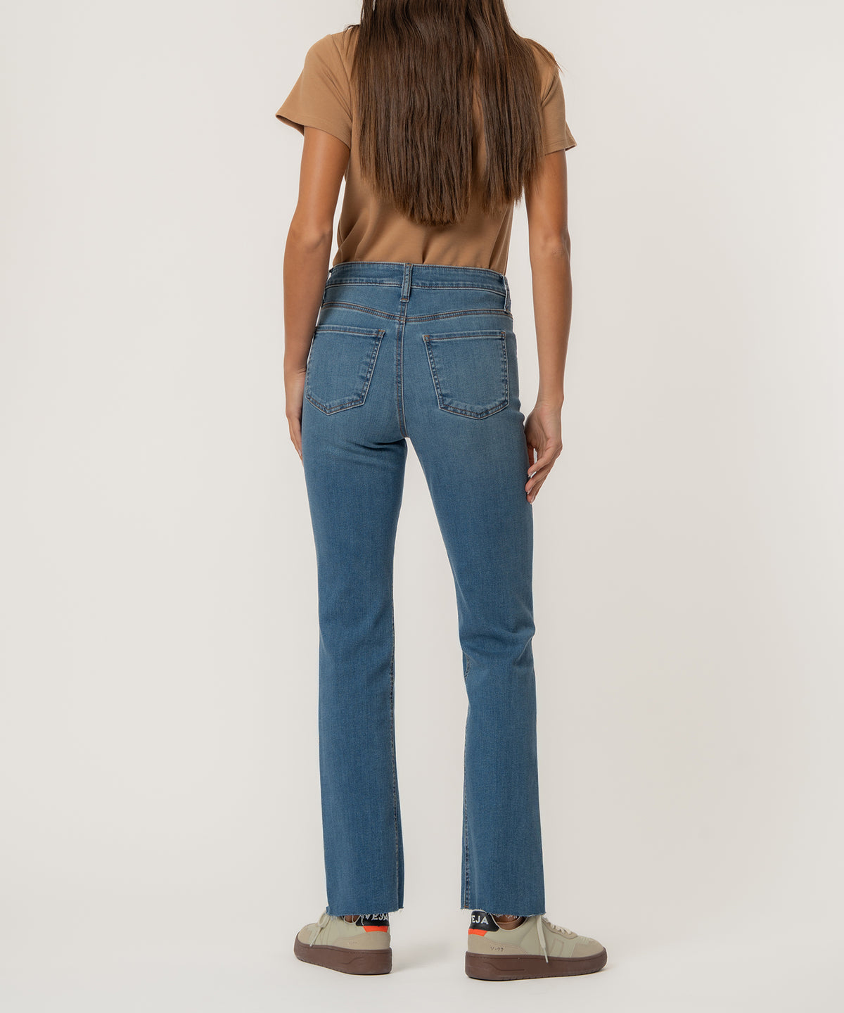 High-rise blue flare jeans with a raw hem, shown from the back with a tan t-shirt.