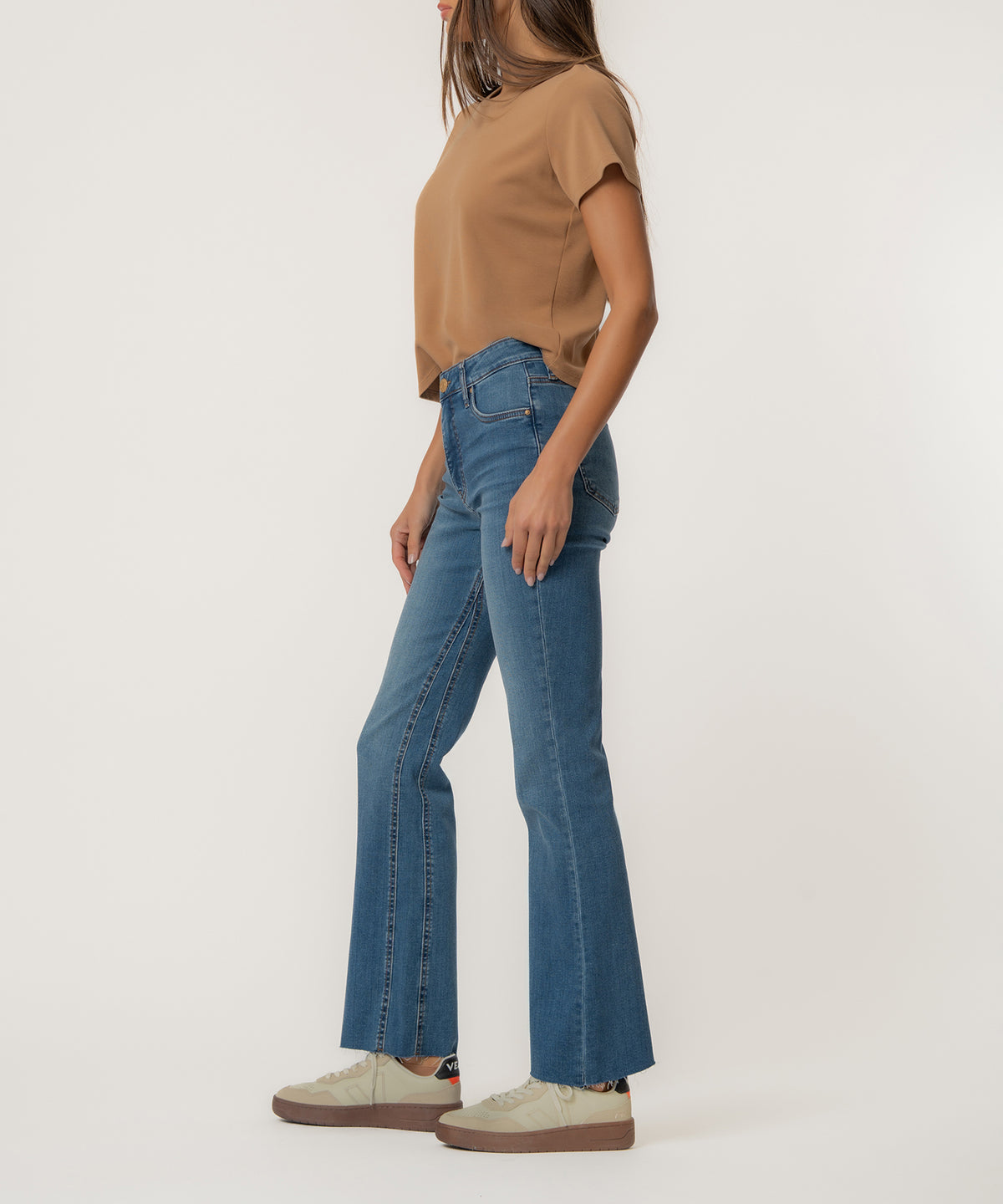 Woman wearing high-rise flare jeans in medium blue denim with a tan short-sleeved top.