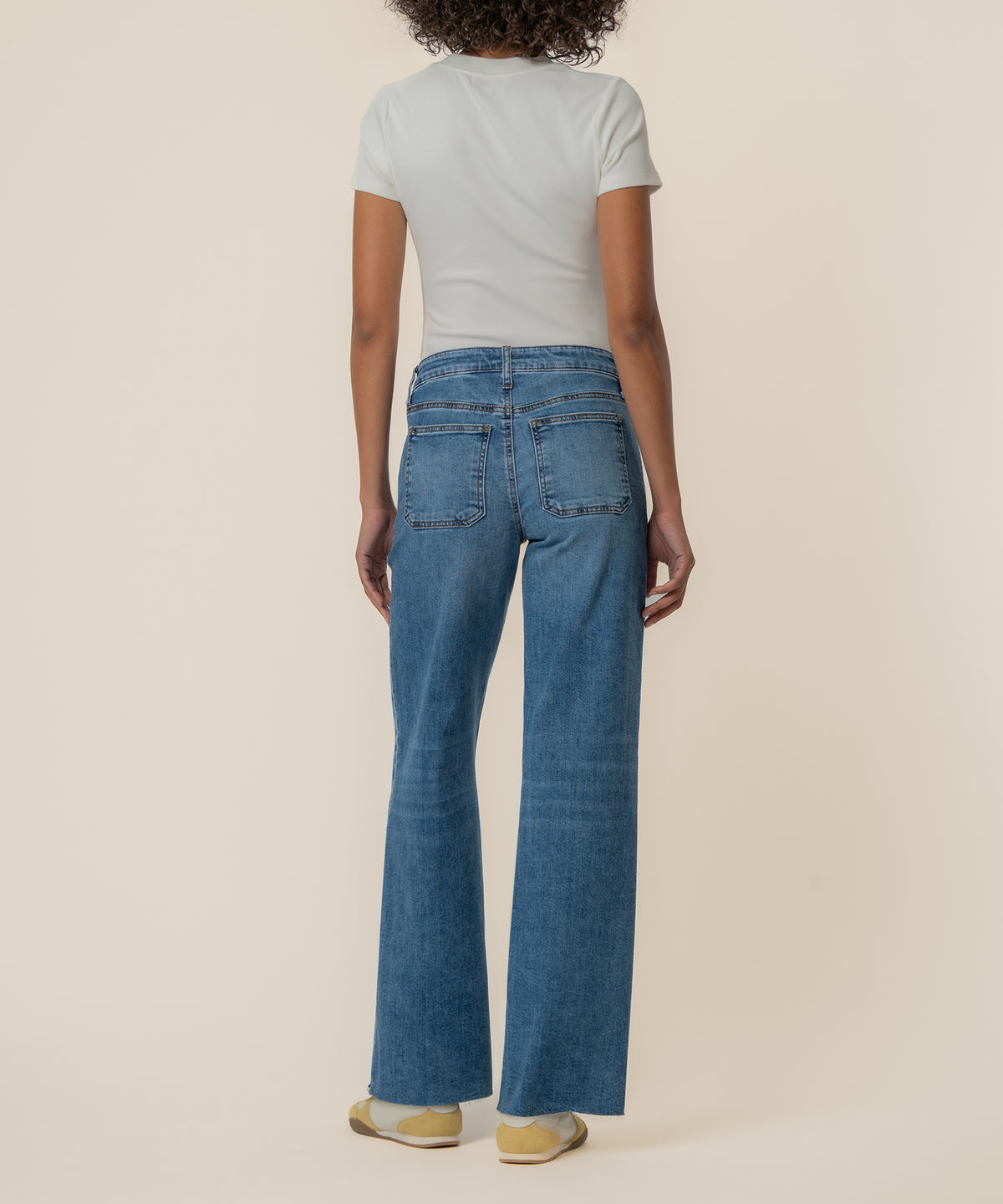 Woman wearing high-rise wide-leg jeans in medium blue denim with back pockets, paired with white t-shirt.