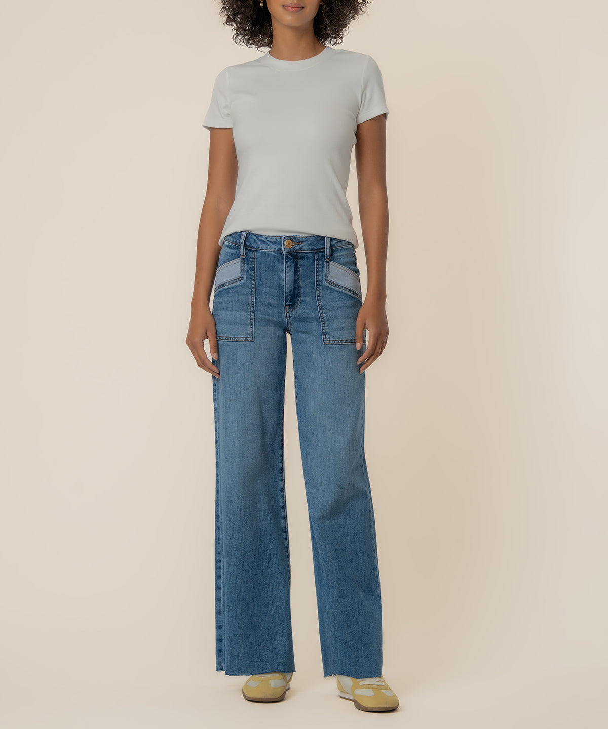 Woman wearing light gray t-shirt and blue high-rise wide-leg jeans with contrast pocket details.