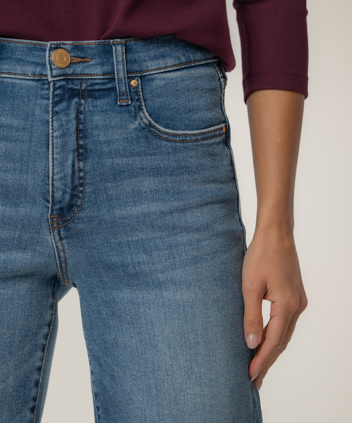 Light blue denim high-rise straight leg jeans with brass button and five-pocket styling worn with burgundy ribbed sweater.
