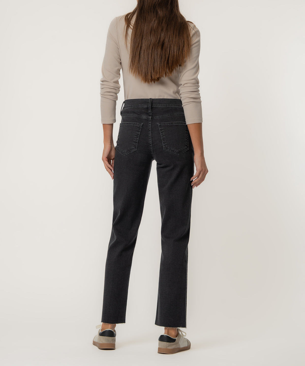 Woman wearing black high-rise straight leg jeans with cream long-sleeve top, viewed from behind.