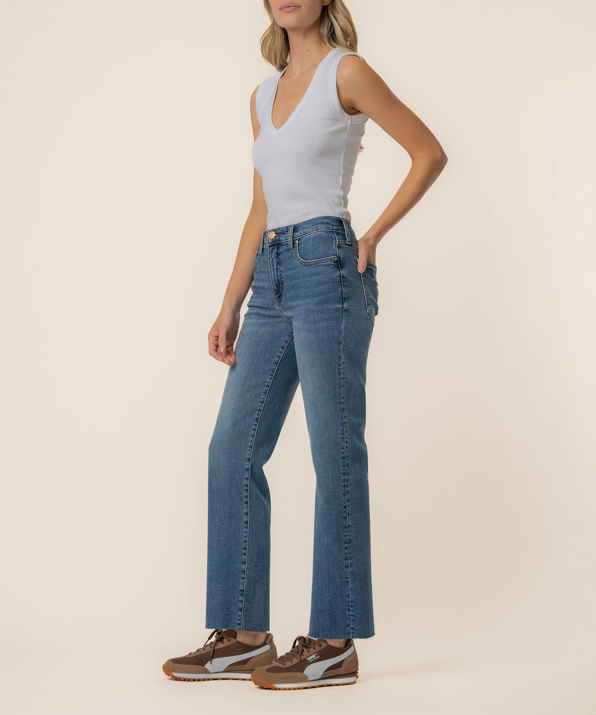 Woman wearing light blue sleeveless v-neck top and medium-wash high-rise straight-leg jeans with brown and white sneakers.