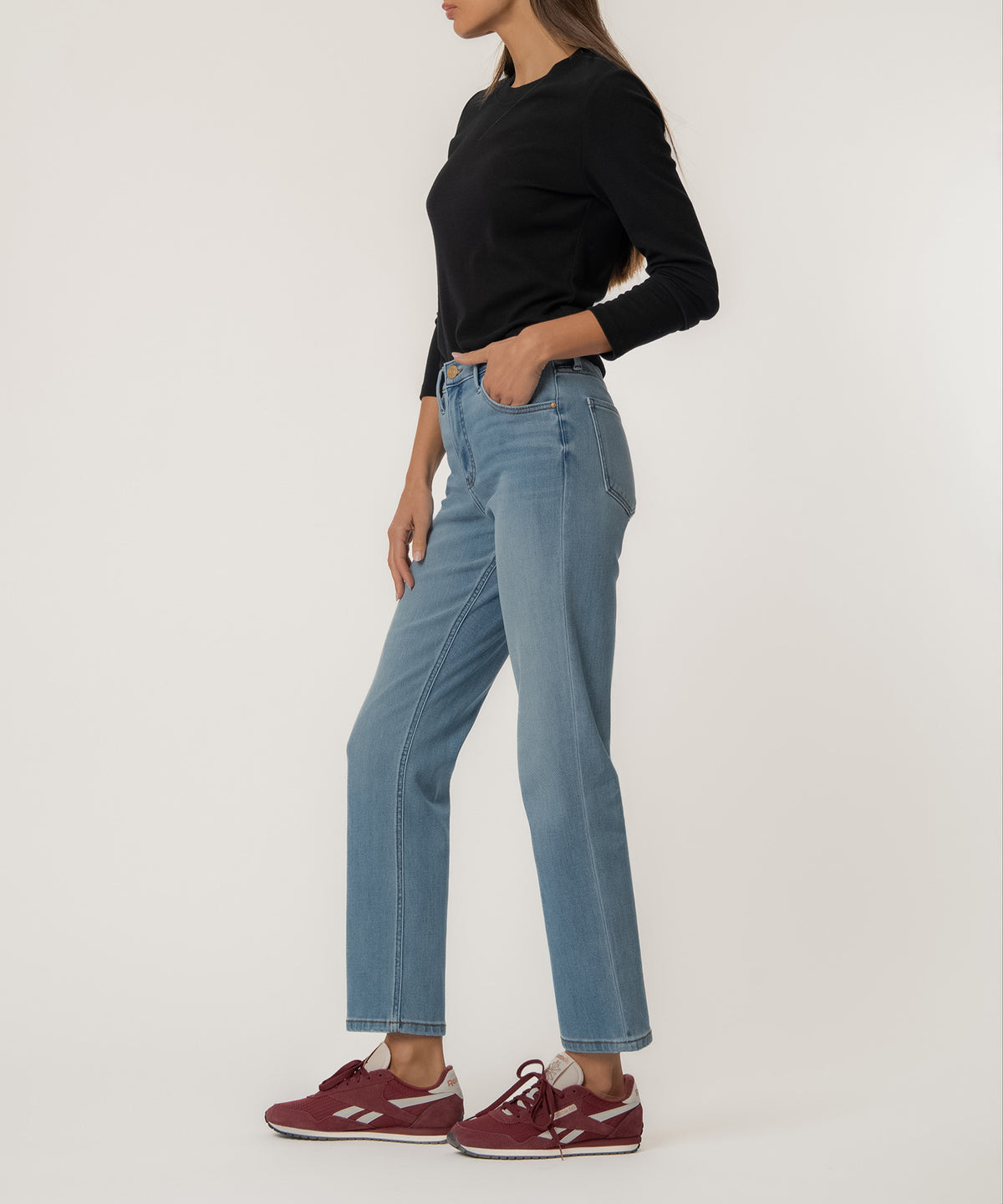 Woman wearing light blue high-rise straight leg jeans with black long-sleeve top and burgundy sneakers.