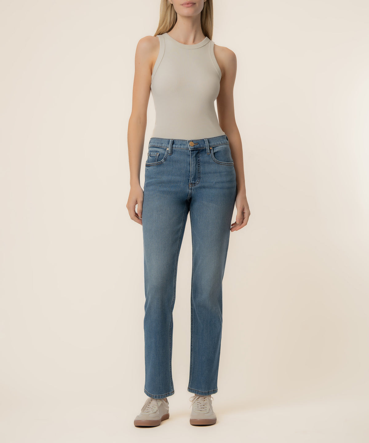 Woman wearing light beige sleeveless tank top and blue high-rise straight-leg jeans with a medium wash.