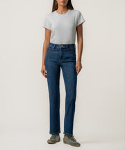 A woman stands facing forward in high-rise dark blue straight-leg jeans, a light gray short-sleeve tee, and olive green sneakers.