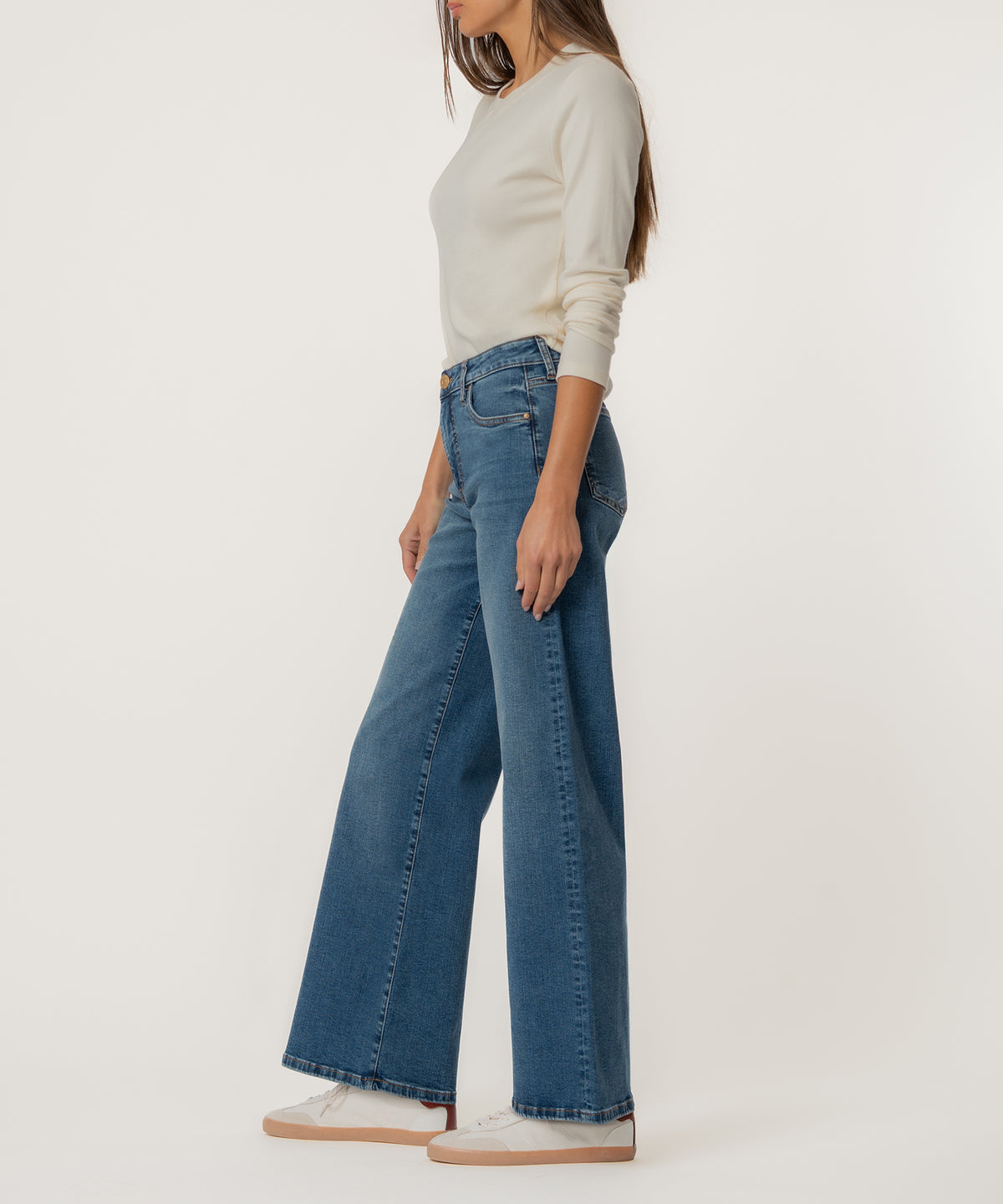 Woman wearing cream long-sleeve top and blue high-rise wide-leg jeans with raw hem, viewed from the side.