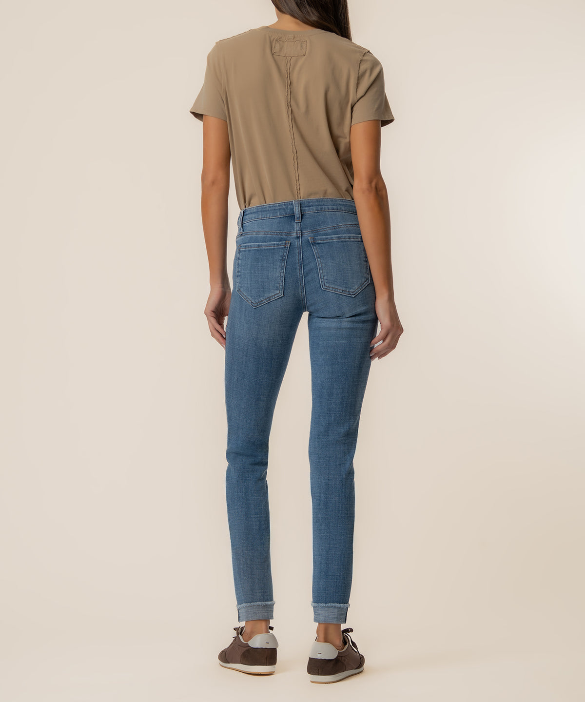 Woman wearing medium-wash straight-leg crop jeans with rolled cuffs and a tan short-sleeve top, back view.