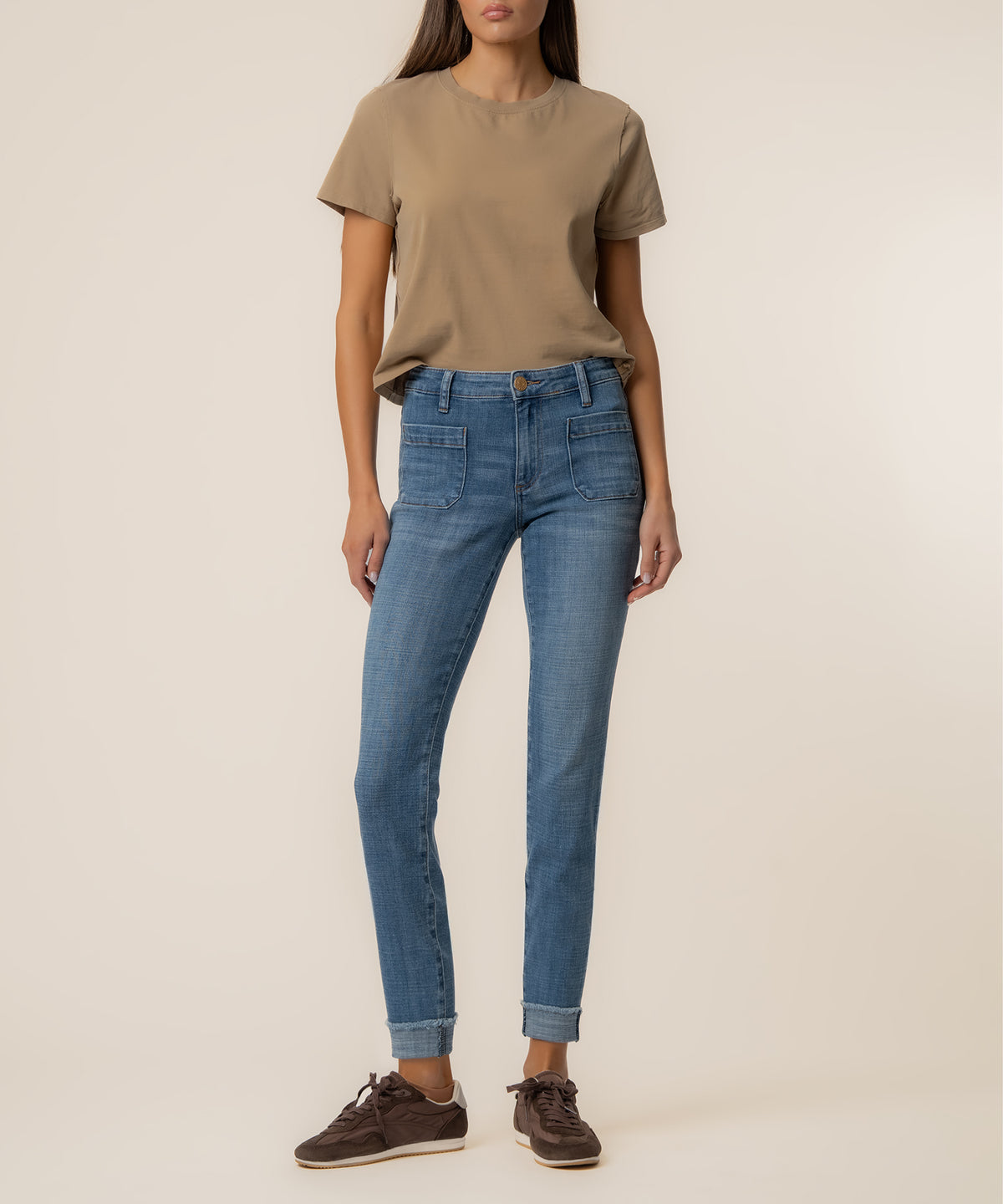 Woman wearing beige t-shirt and blue straight-leg jeans with cuffed ankles.