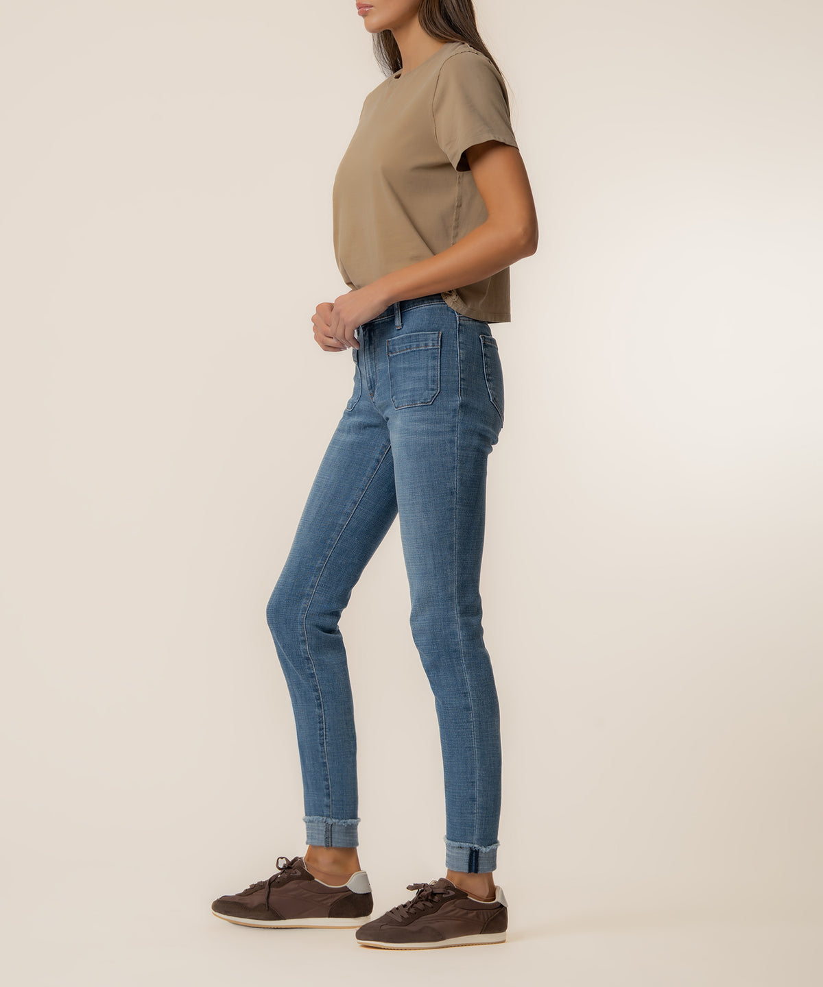 Woman wearing blue straight leg jeans with cuffed ankles and a tan short-sleeve shirt.