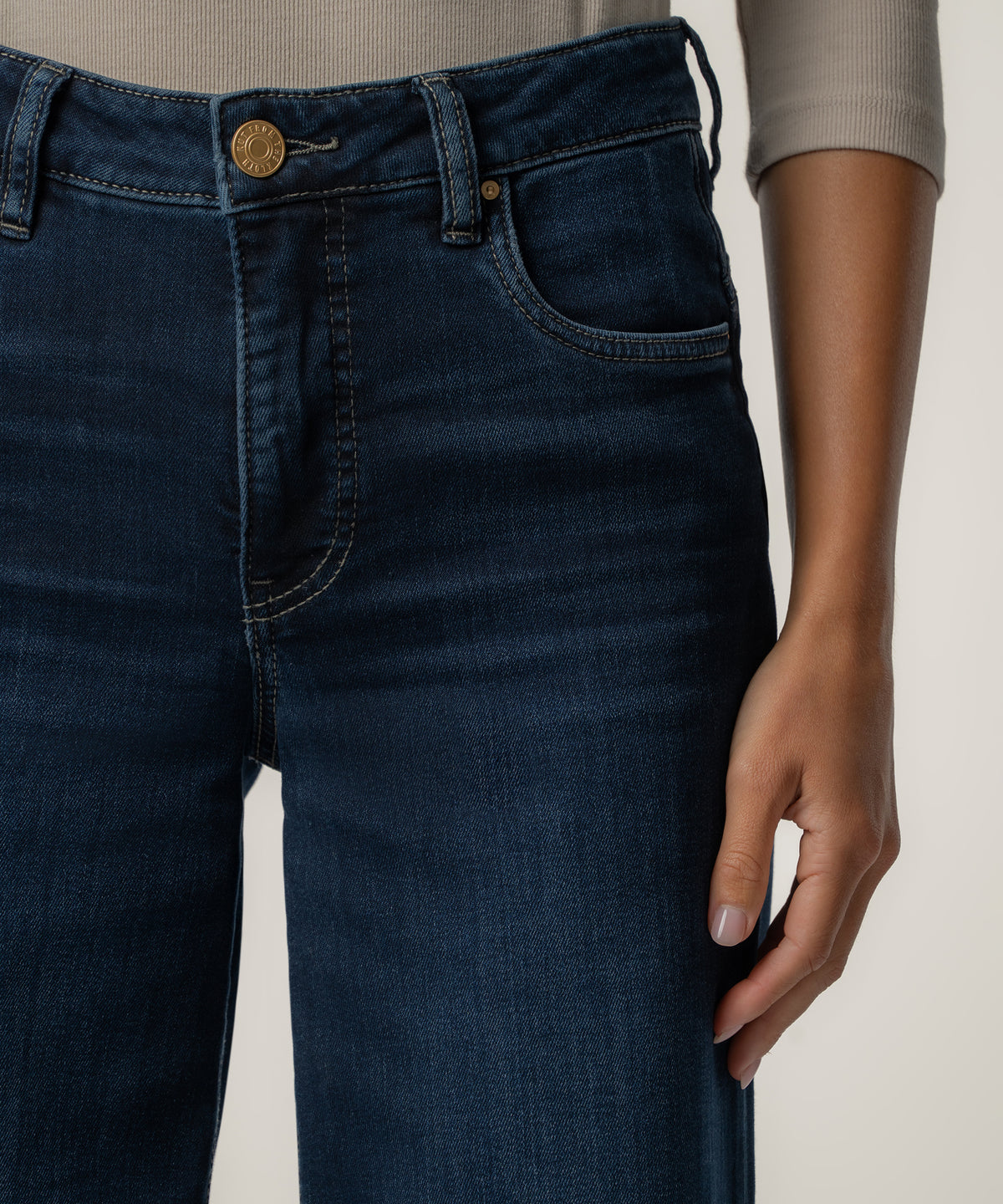 Close-up of a person wearing dark indigo high-rise wide-leg jeans with a gold button, paired with a gray ribbed long-sleeve top.