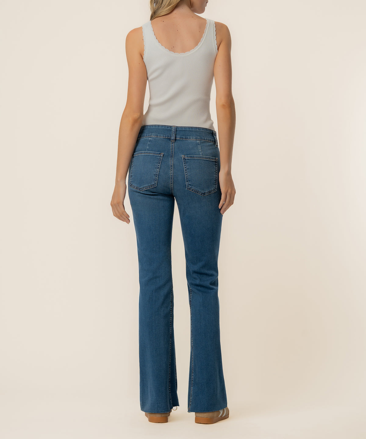 Woman wearing high-rise flare jeans in medium blue wash with white ribbed tank top, rear view.