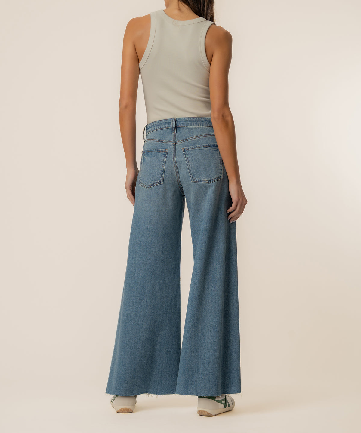 Woman wearing a cream sleeveless tank top and light blue high-rise wide-leg jeans with a frayed hem.