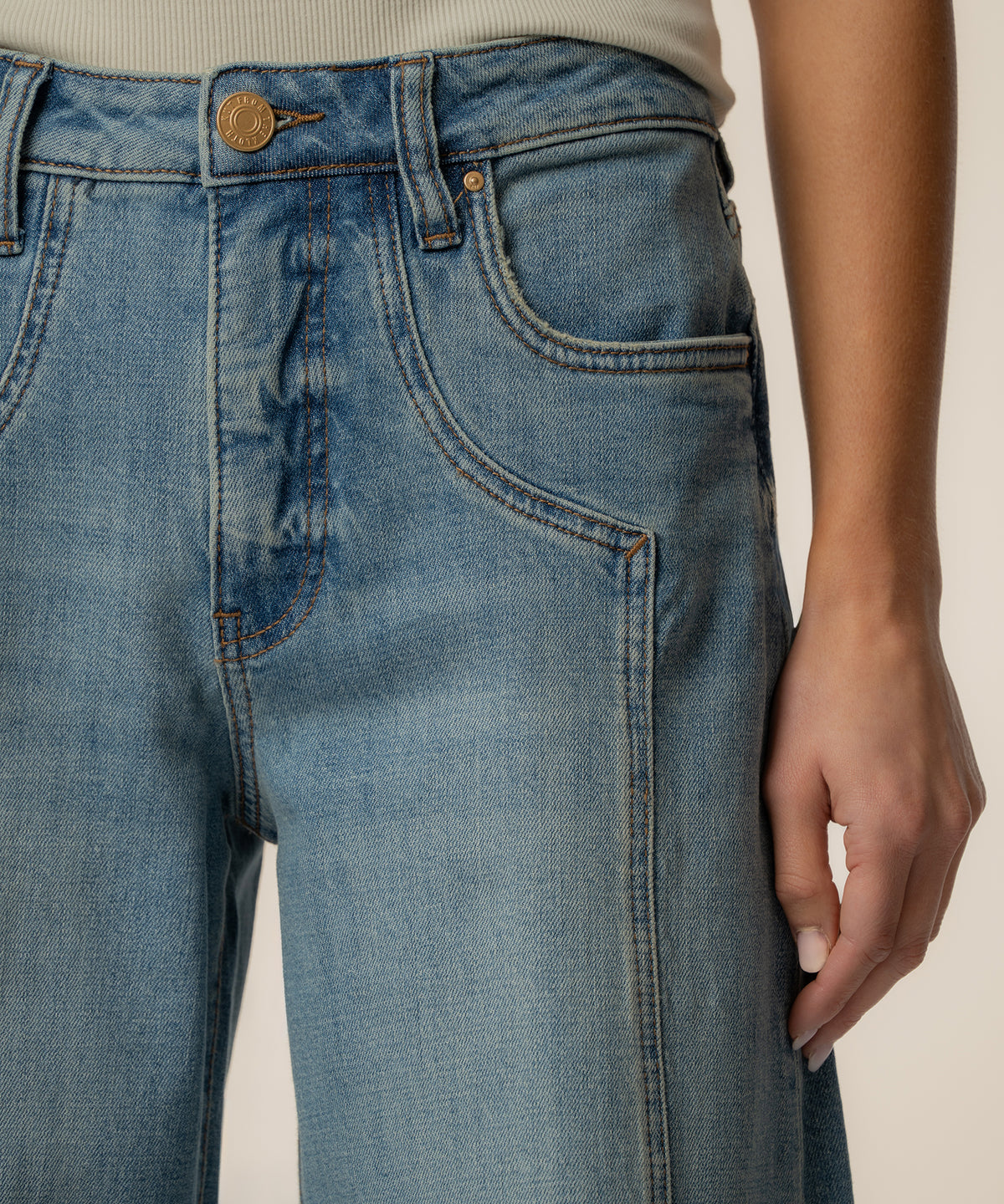 Light blue high-rise jeans with wide legs, gold button, and five-pocket styling shown at waist and thigh.