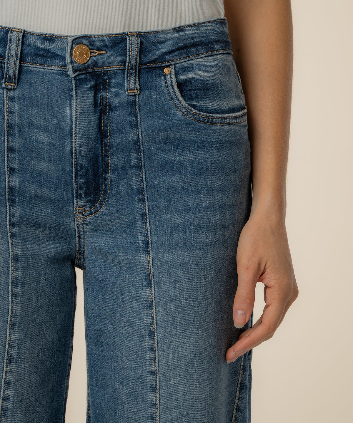 High-rise blue jeans with wide straight legs, gold button, and front pockets visible on model.